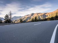 a curve road with a mountain in the distance and trees and mountain peaks in the background