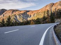 a curve road with a mountain in the distance and trees and mountain peaks in the background