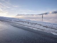 a street covered in snow next to a mountain side road and telephone poles and mountain range