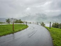 a road with a fence in a rainy day, with grass and mountains in the distance