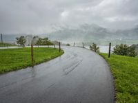 a road with a fence in a rainy day, with grass and mountains in the distance