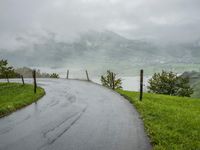 a road with a fence in a rainy day, with grass and mountains in the distance