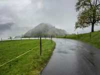 a road with a fence in a rainy day, with grass and mountains in the distance