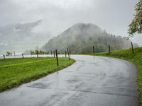 a road with a fence in a rainy day, with grass and mountains in the distance
