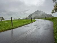 a road with a fence in a rainy day, with grass and mountains in the distance