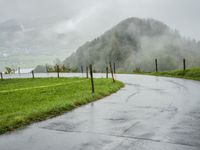 a road with a fence in a rainy day, with grass and mountains in the distance