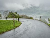 a road with a fence in a rainy day, with grass and mountains in the distance