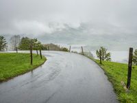 a road with a fence in a rainy day, with grass and mountains in the distance