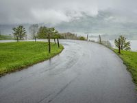 a road with a fence in a rainy day, with grass and mountains in the distance