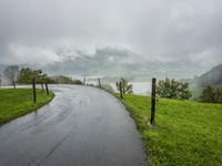 a road with a fence in a rainy day, with grass and mountains in the distance