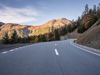 a curve road with a mountain in the distance and trees and mountain peaks in the background