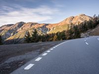 a curve road with a mountain in the distance and trees and mountain peaks in the background