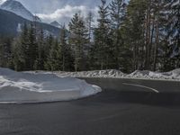 the asphalt road curves around a snowy slope and trees line the road in front of it