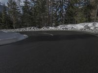 the asphalt road curves around a snowy slope and trees line the road in front of it
