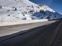 a road that is next to a mountain covered in snow while the sun shines