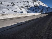 a road that is next to a mountain covered in snow while the sun shines