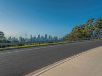 the road is empty as a view of a city in the distance, with trees and buildings lining both sides