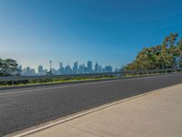 the road is empty as a view of a city in the distance, with trees and buildings lining both sides