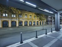 there is an empty street with yellow buildings on the other side of the road at night