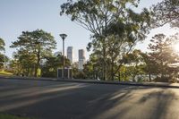 a street that has some trees in it and buildings behind it and a person sitting on one side of the road with a skateboard