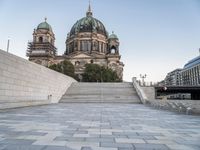 there is a large building with three domes and steps to it's left, with an empty concrete patio on the right