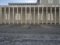 some columns outside a building with buildings on the other side of them, and sun shining over them