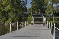 a dock that is connected to a pond and some trees behind it with a white fence