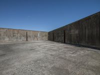 an empty lot with concrete walls against a blue sky background with one small skateboard leaning against a fence