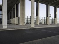 a long line of pillars stands at an airport terminal and there is a lone person walking underneath