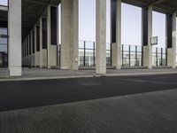 a long line of pillars stands at an airport terminal and there is a lone person walking underneath