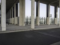 a long line of pillars stands at an airport terminal and there is a lone person walking underneath