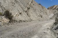 a man riding on a motorcycle through a large canyon area on a rocky road with a rock wall behind him