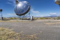 two large metal telescopes in a desert area near water and a building and some grass