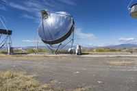 two large metal telescopes in a desert area near water and a building and some grass