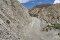 a person riding a bike up a hill on a gravel road in front of a mountain side