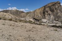 a group of brown mountains in the middle of a desert with rocks and weeds all around