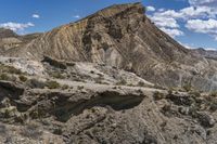 a group of brown mountains in the middle of a desert with rocks and weeds all around