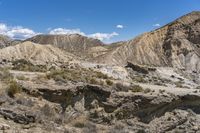 a group of brown mountains in the middle of a desert with rocks and weeds all around