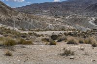 the top of a hill surrounded by hills and shrubs in the desert, and road with steeps