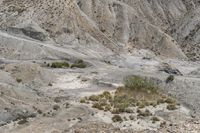 a man rides a motorcycle through a canyon in death valley national park, nevada, with steep mountains behind him