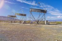 large set of satellite dishes sitting in the middle of an empty field under a blue sky