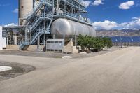 a huge silver tank sitting in front of a power station near the water's edge