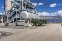 a huge silver tank sitting in front of a power station near the water's edge