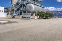 a huge silver tank sitting in front of a power station near the water's edge