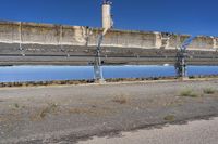 a large metal structure reflecting in water with a cement wall behind it, with another big structure on the opposite side