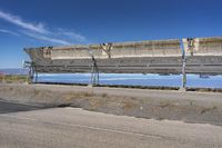 large metal structure in desert by the water reflecting sky and clouds against blue sky with grass and dirt