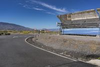 a view of the empty road next to the mountains with a bench on top, on a sunny day