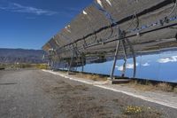 a person in black walking in front of a large solar panel on a road with mountains in the background