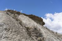 a steep face with grass growing along the side, above rocks, in the distance is a blue sky