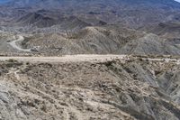 a truck traveling down a winding road in mountains and desert terrain below a mountain range